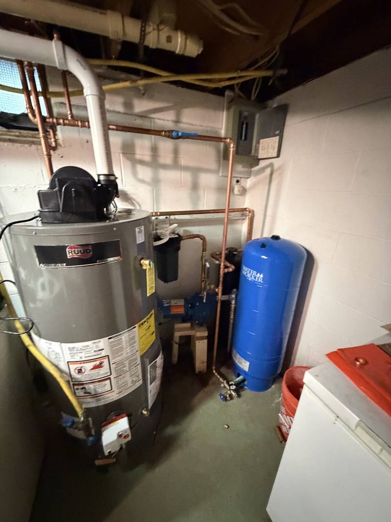 Gas water heater, copper piping and blue well pressure tank in a basement