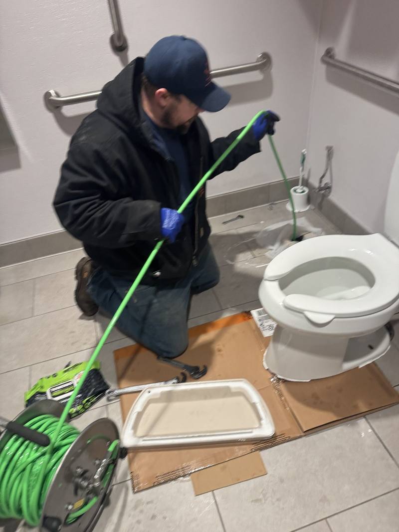 Plumber feeding a drain snake into a toilet drain in a commercial restroom