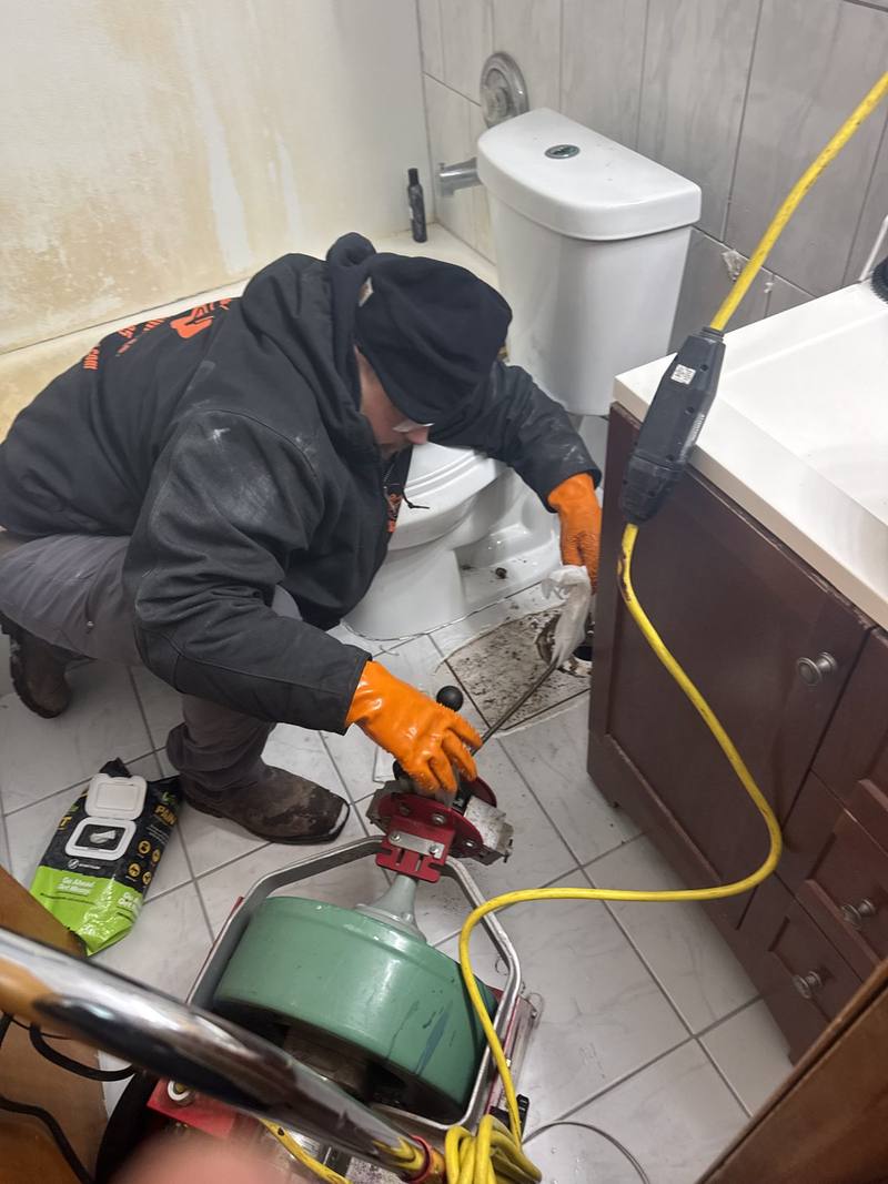 Plumber using a drain machine to clear a bathroom floor drain