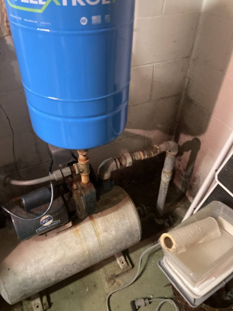 Well pump and pressure tank with galvanized piping in a basement