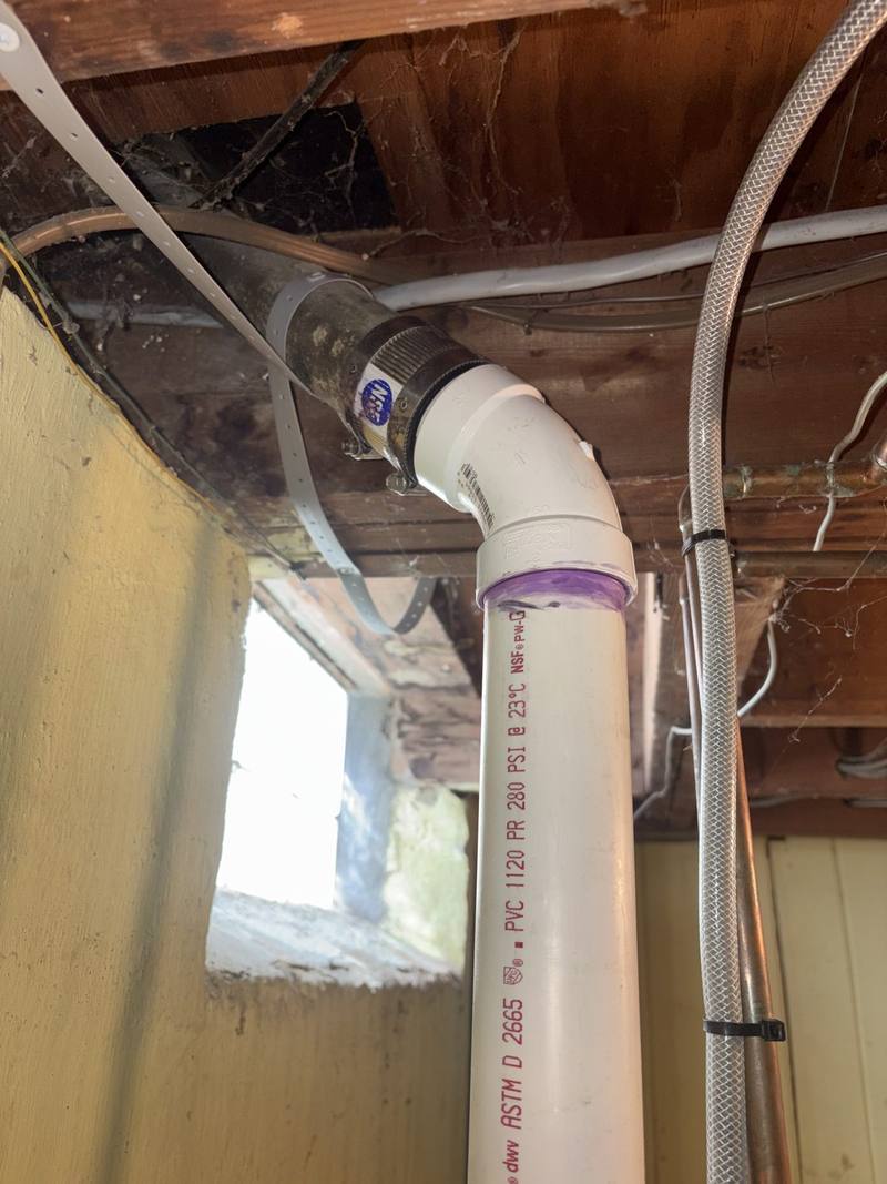 New white PVC pipe and fitting connected to an existing line under basement joists