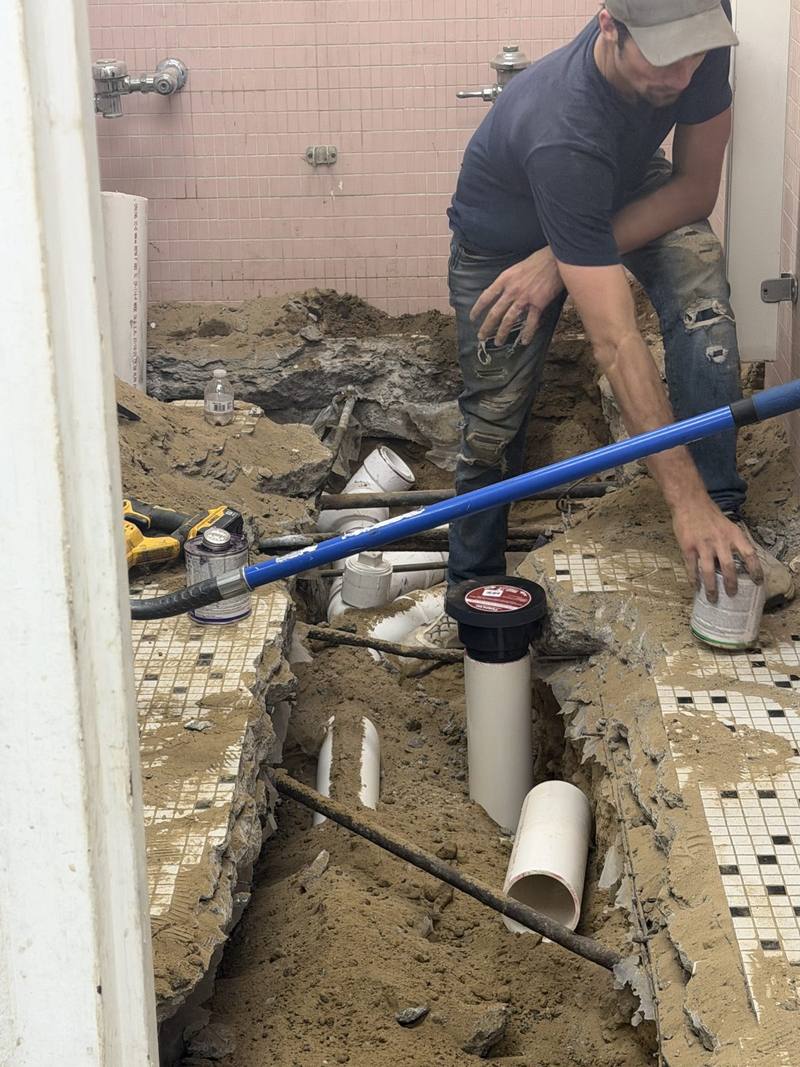 Plumber replacing underground drain lines beneath a commercial restroom floor