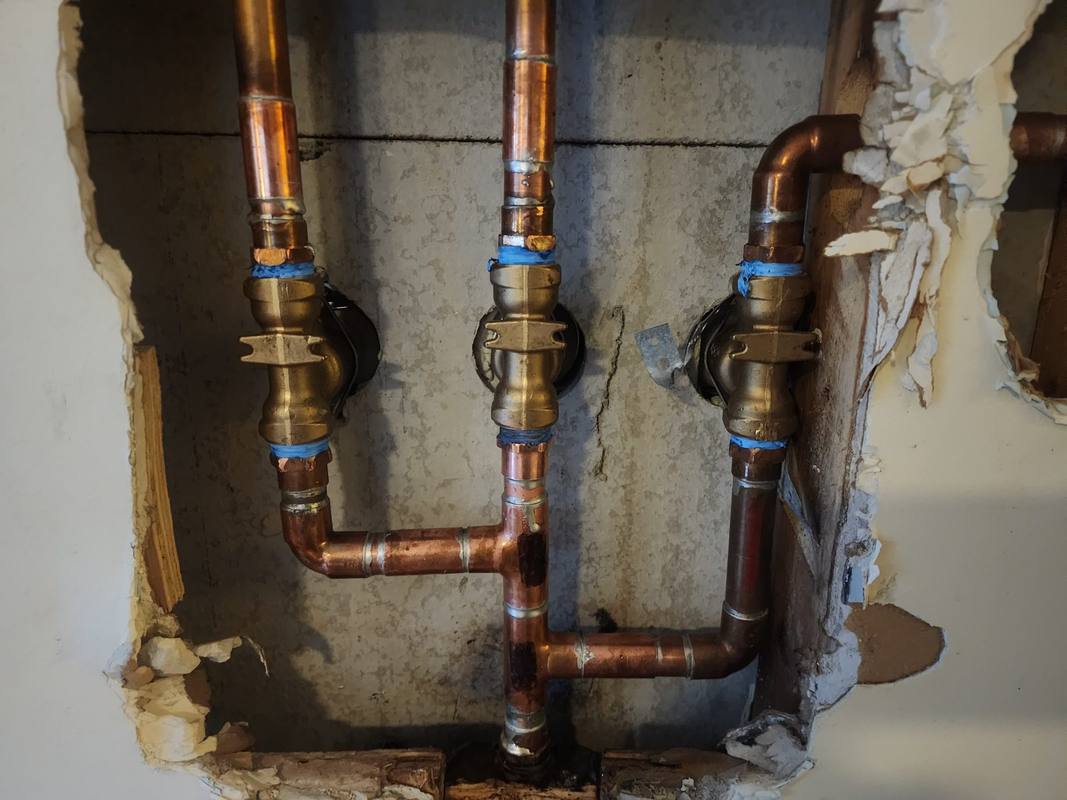 Three brass shutoff valves on new copper piping inside a wall