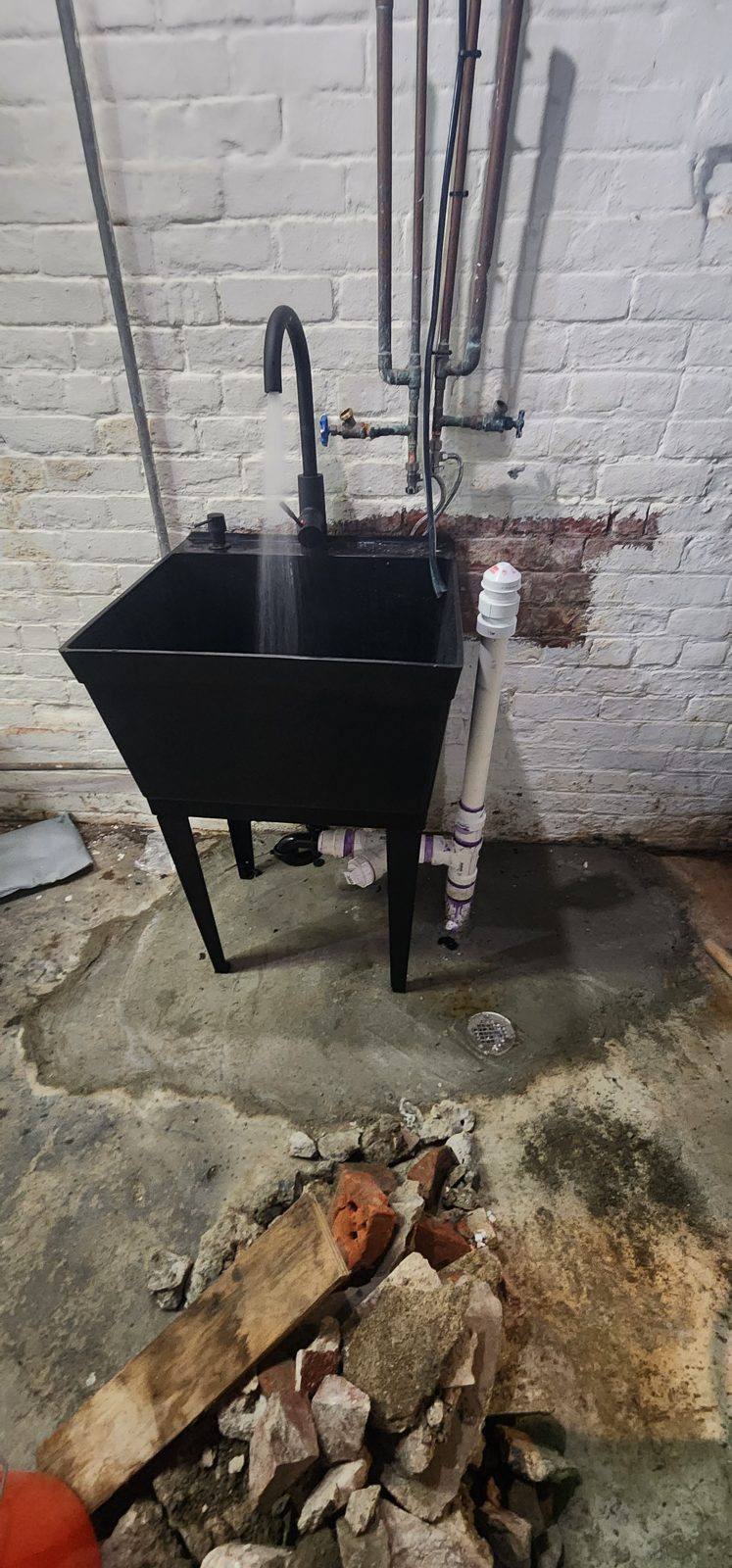 New black utility sink with faucet and white PVC drain in a basement